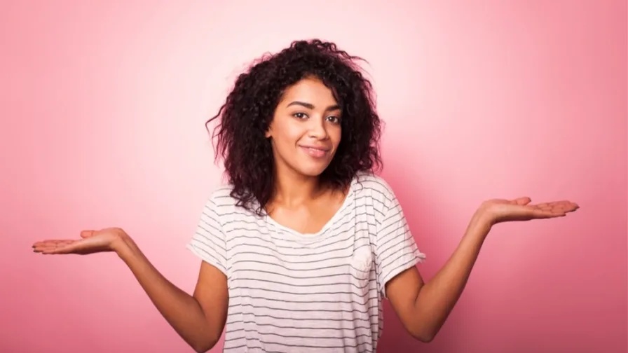 Woman shrugging shoulders in front of pink background